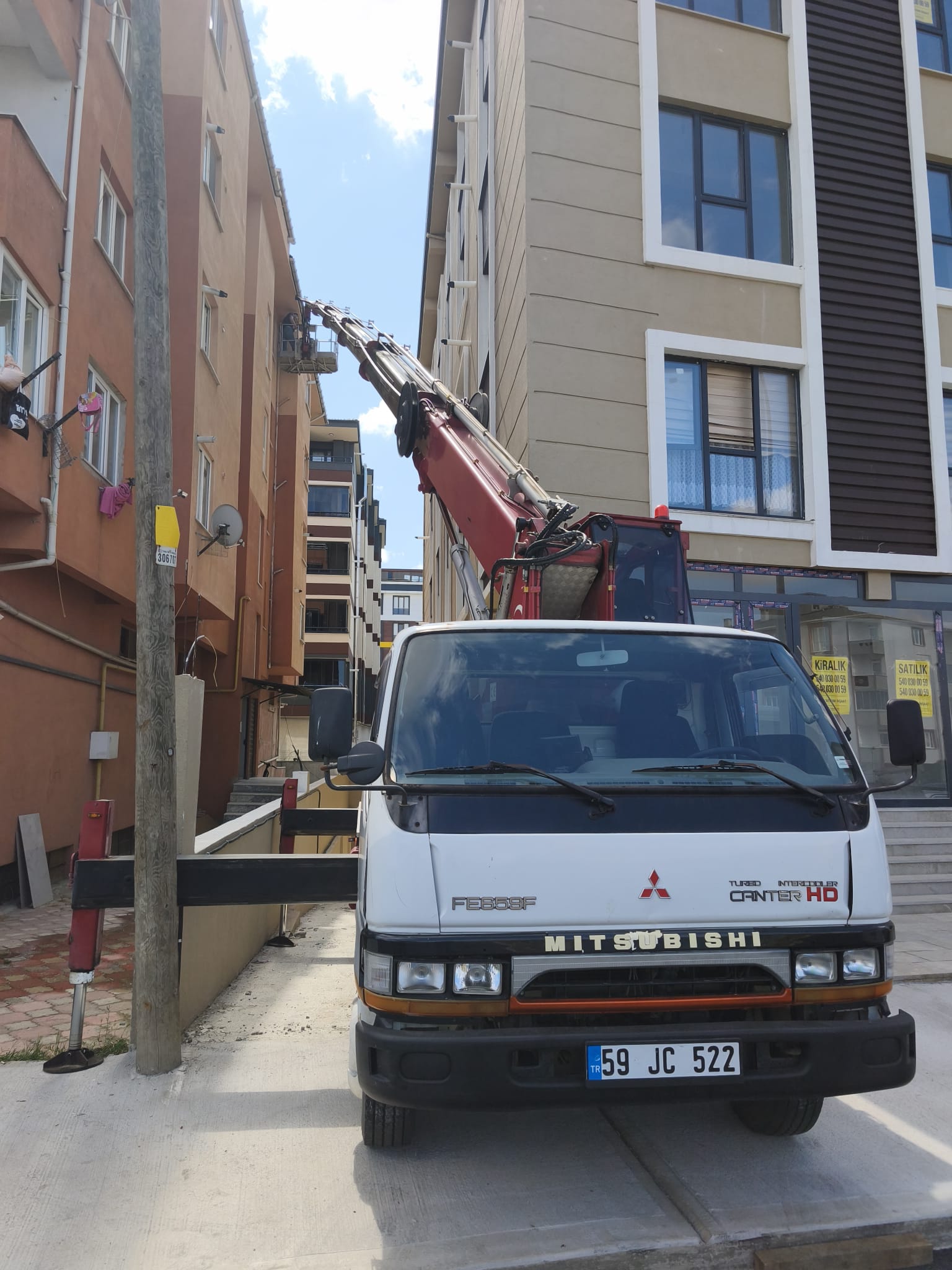 Dar sokakta beyaz kamyonlu sepetli vinç çalışması