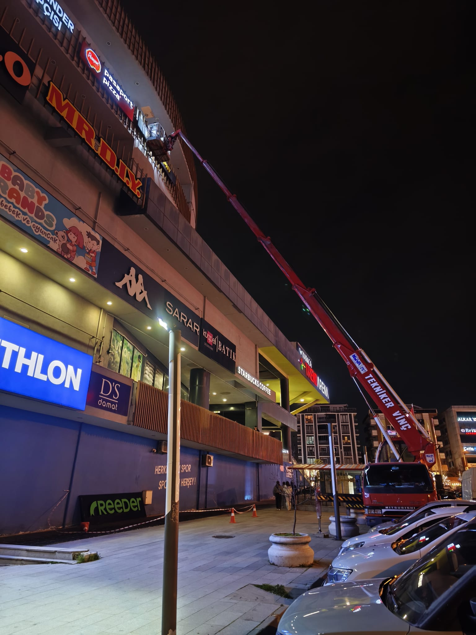 Gece mağaza tabelasına uzanan sepetli vinç