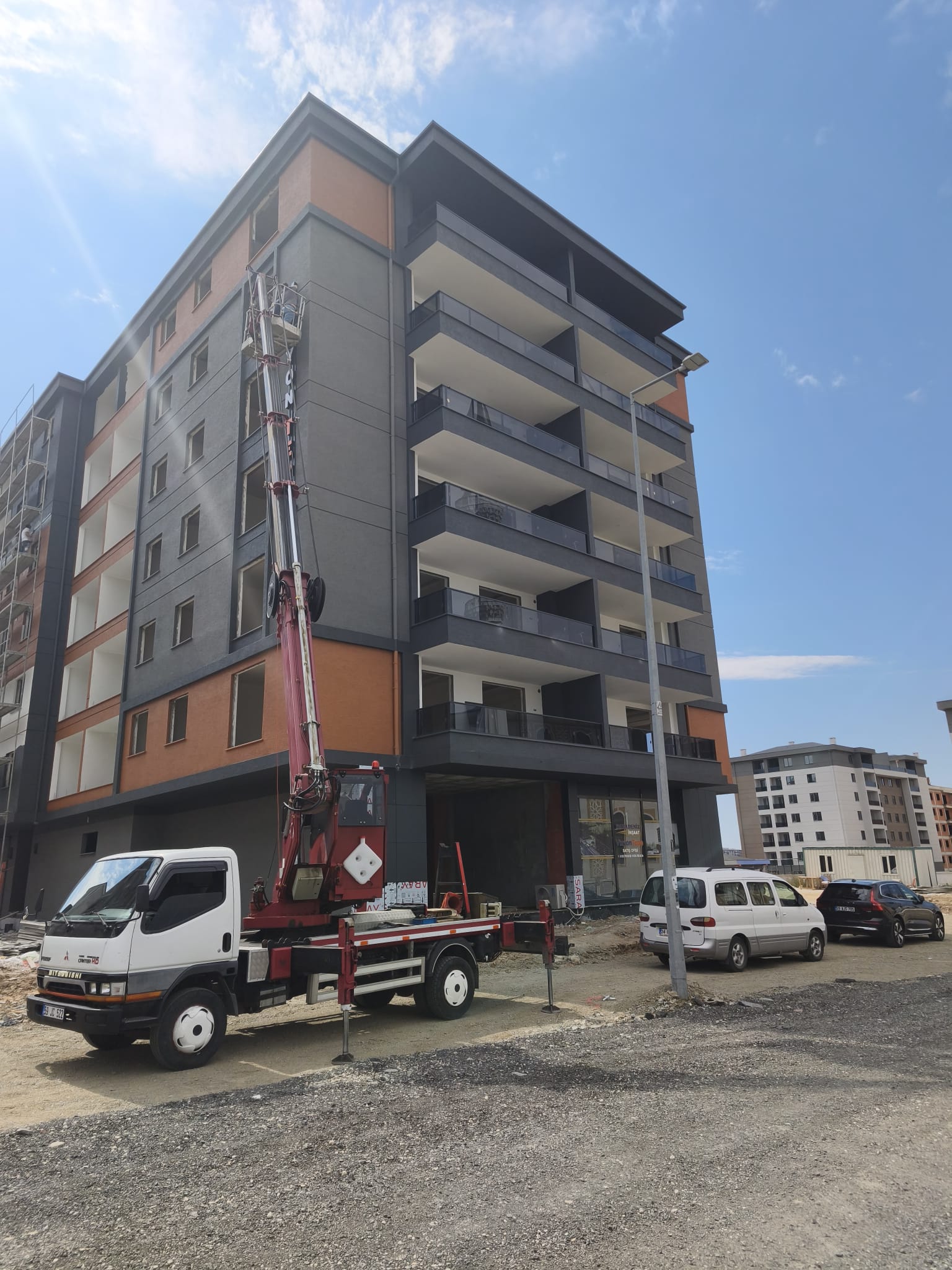 Gri ve turuncu apartman cephesinde sepetli vinç