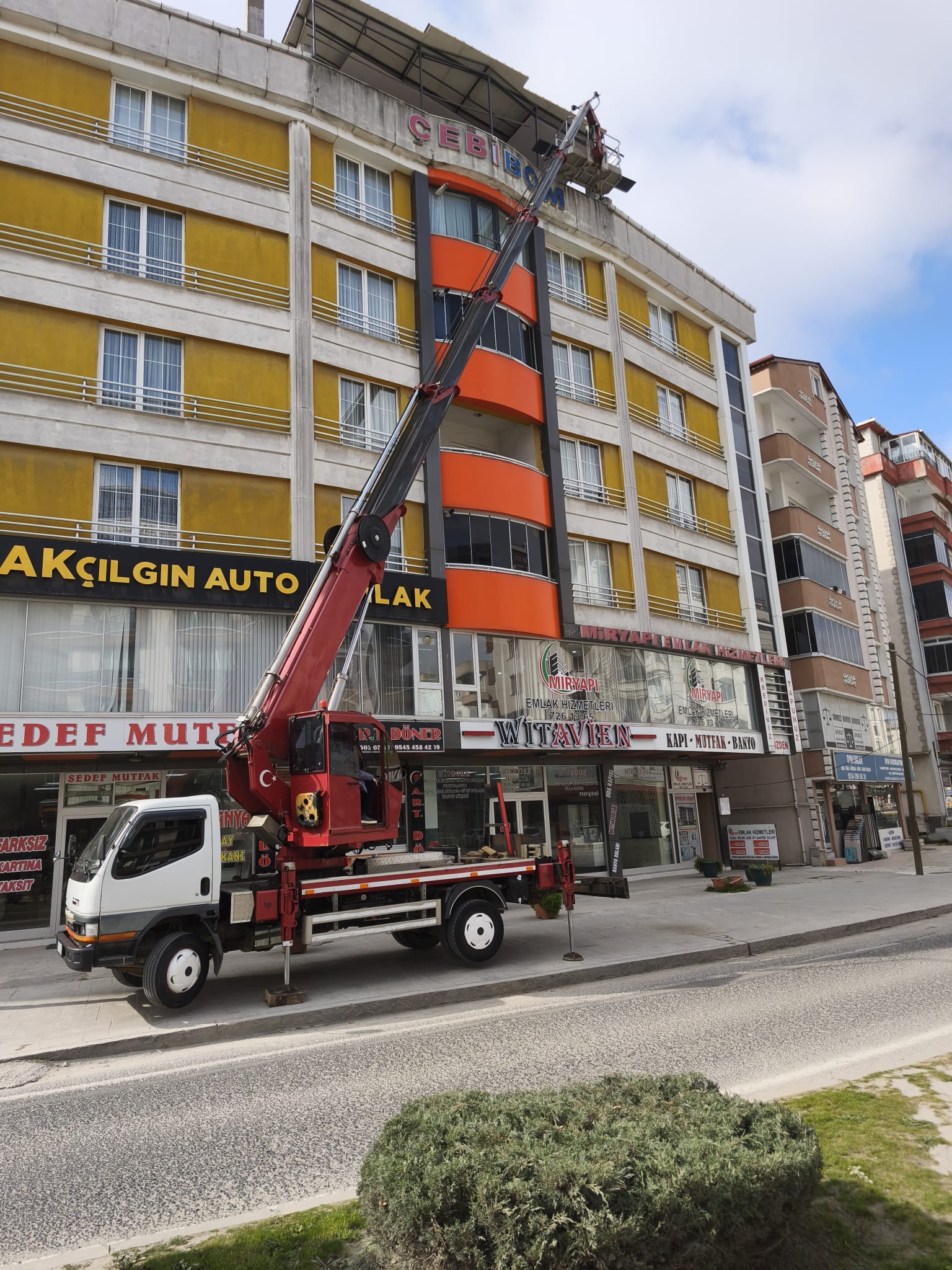 Sarı ve turuncu apartmanın çatısına uzanan sepetli vinç