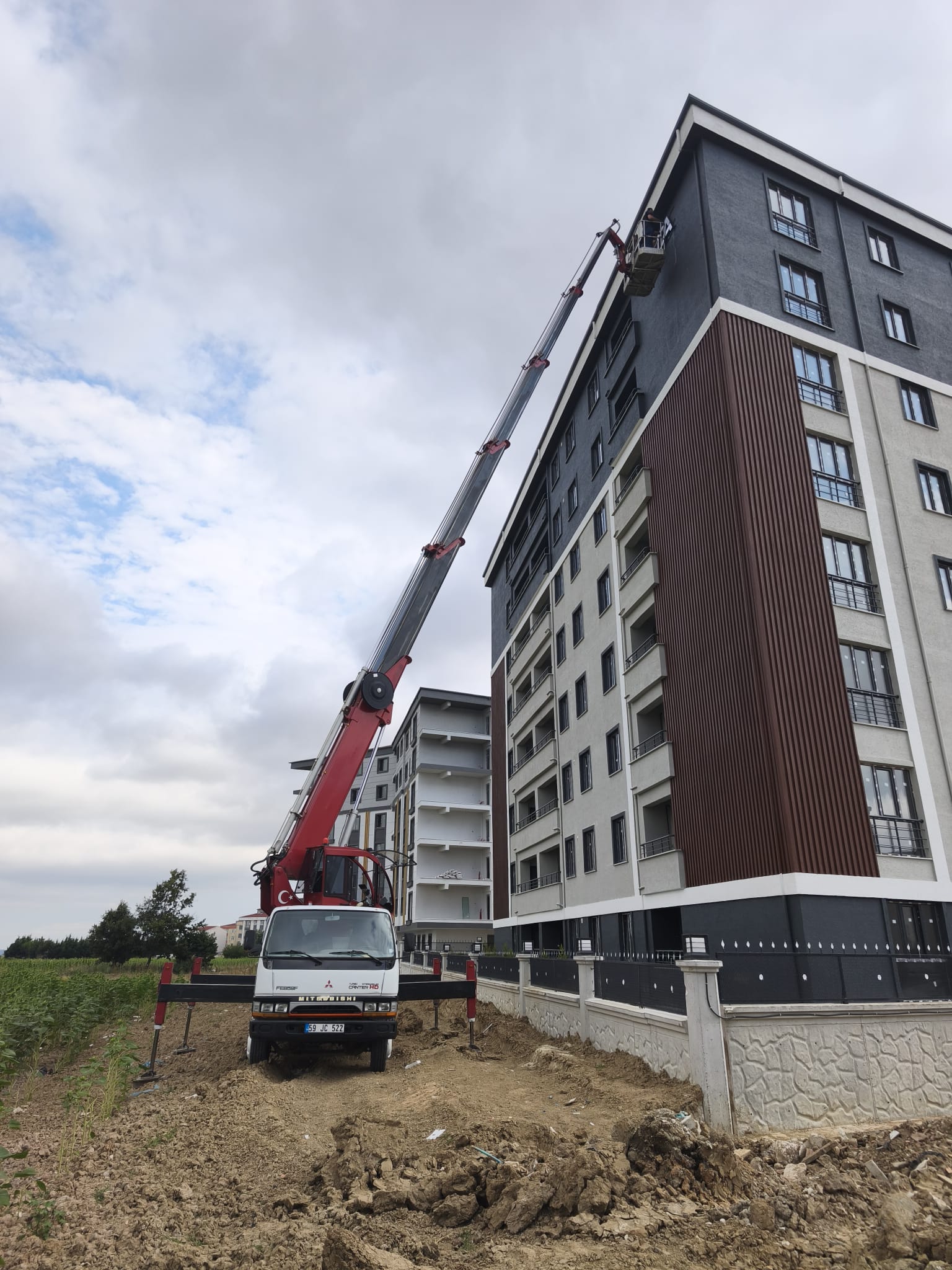 Toprak zeminde yüksek apartmana uzanan sepetli vinç